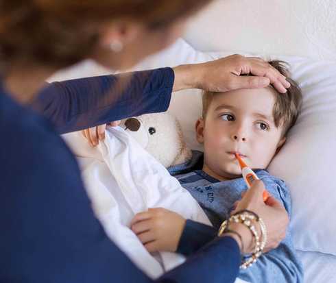 Mutter fühlt Stirn ihres Sohnes und hält ihm ein Fieberthermometer in den Mund