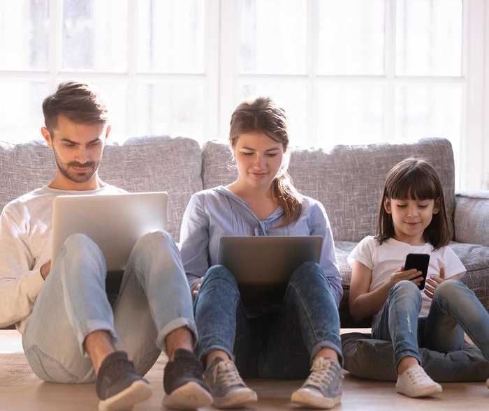Dreiköpfige Familie sitzt auf dem Sofa und jeder schaut auf seinen eigenen Laptop oder das Smartphone