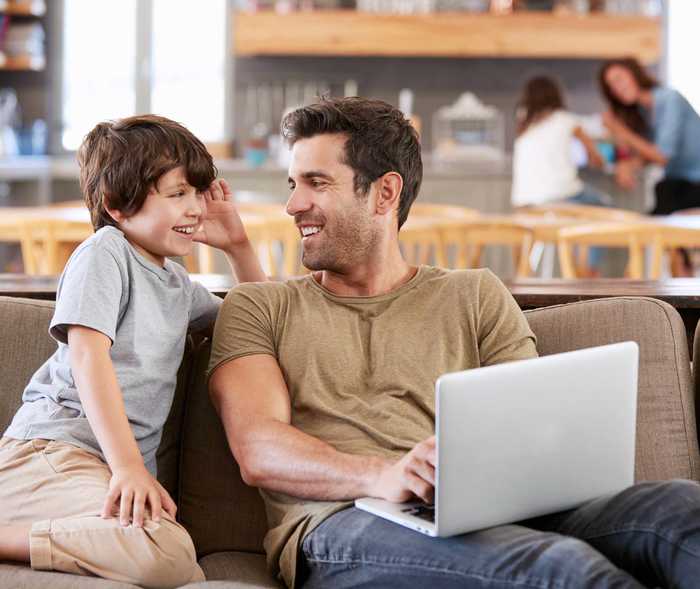 Vater lacht mit seinem Sohn vor einem Laptop