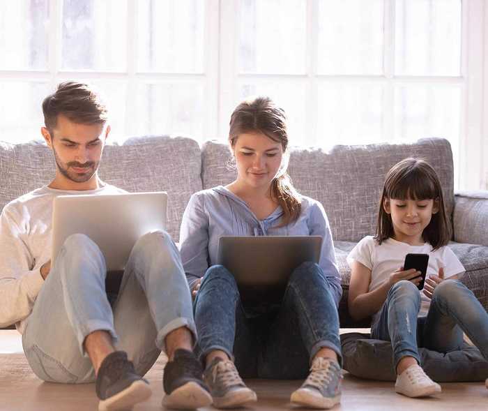 Familie sitzt auf dem Sofa und jeder schaut auf seinen eigenen Laptop oder Smartphone