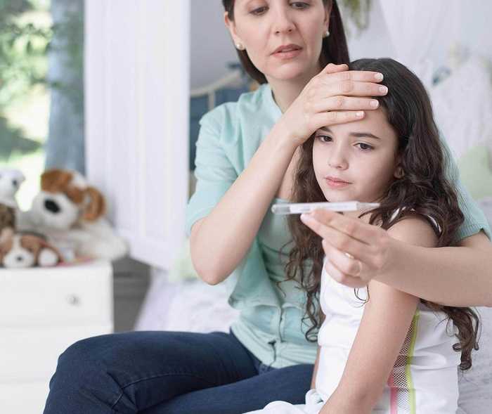 Mutter fühlt Stirn ihrer Tochter und schaut auf ein Fieberthermometer