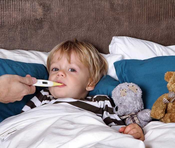 Ein Junge im Bett mit Fieberthermometer im Mund