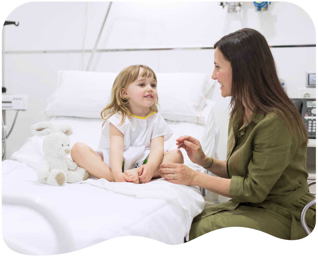 Mädchen sitzt im Krankenhausbett und lacht mit ihrer Mutter